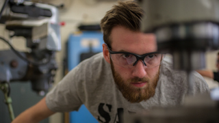 A student is working at a drill station in the NMT Mechanical Engineering Machine Shop.